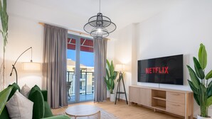 Un soggiorno moderno con televisione, divano verde e un balcone con tende.