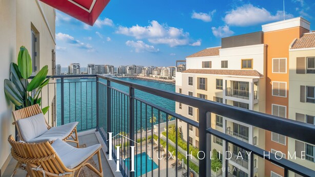 Un balcone con sedie in vimini e vista su un porto turistico e degli edifici.