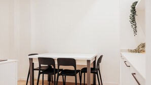 A white dining table with four black chairs, a white cabinet to the left, and a white countertop with a plant to the right.
