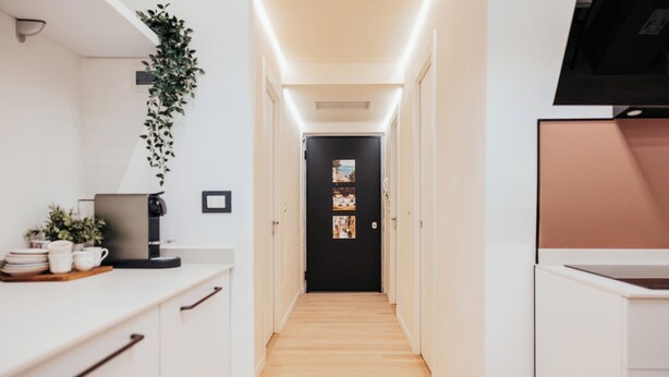 A narrow hallway with a wooden floor, white walls, and a black door at the end.