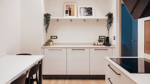A modern kitchen with white cabinets, a white countertop, a black stove, and a hanging plant.
