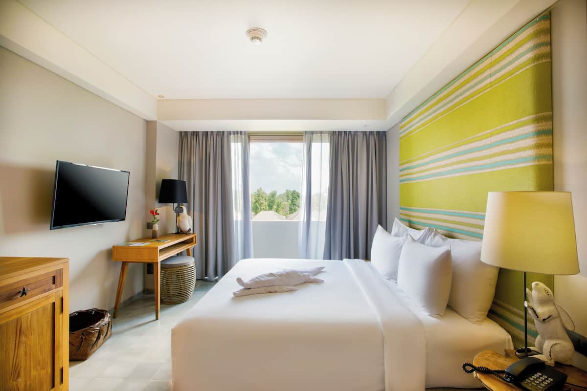 A hotel room with a large bed, a TV, a desk with a lamp, and a view of the outdoors.