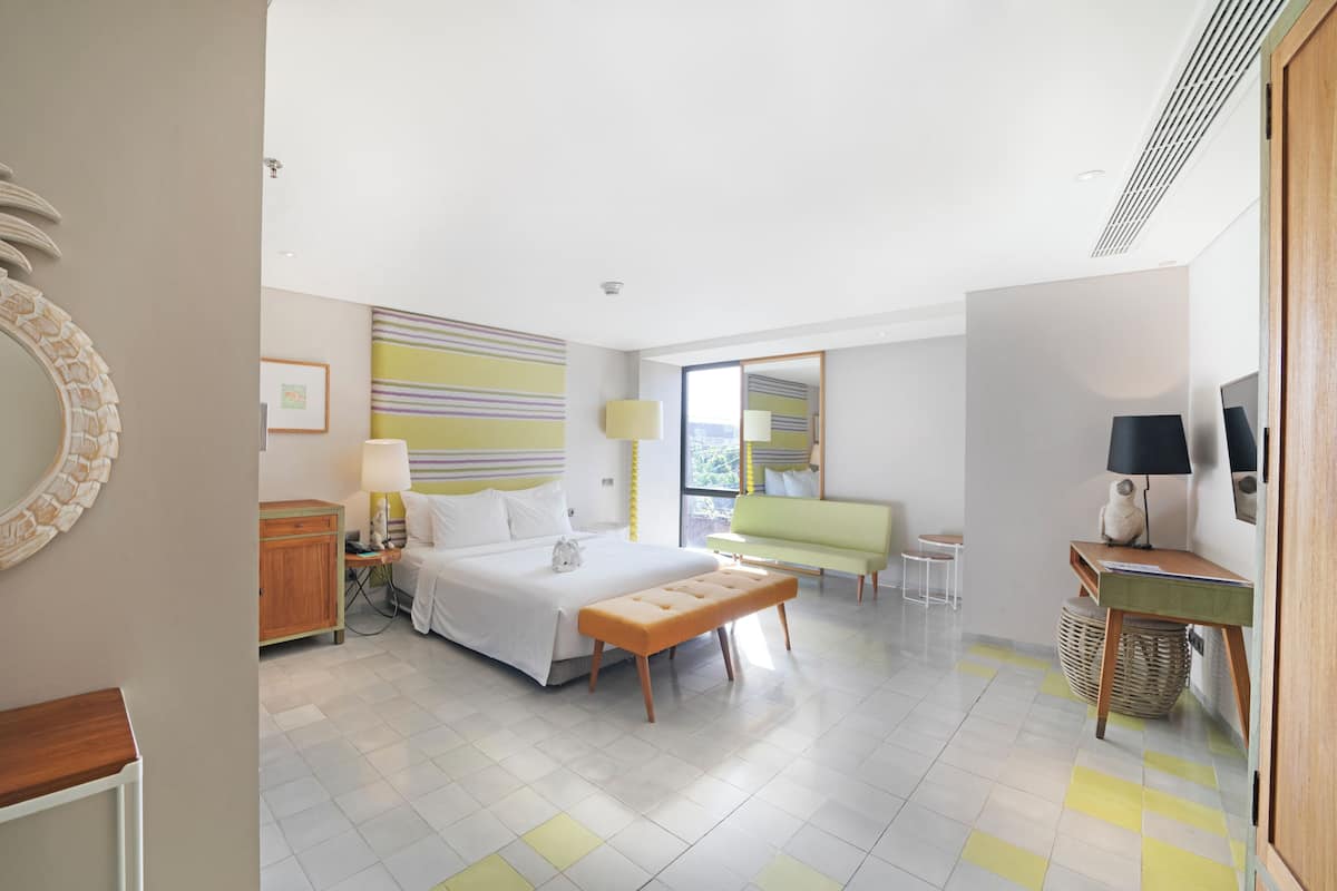A modern hotel room with a bed, bedside table, lamp, and a view of the city.