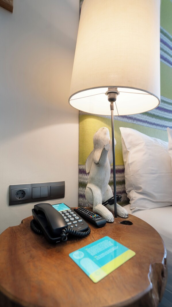 A hotel room with a bed, a nightstand with a lamp, a telephone, and a remote control.