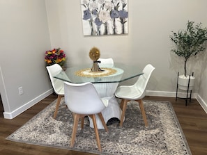 A dining area with a glass-top table, white chairs, a patterned rug, a vase with flowers, and a painting on the wall. - Pet-Friendly & Spacious South Lubbock 3 Bed 2 Bath1 King 2 Queen Near Texas Tech (Lubbock)