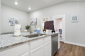 A modern kitchen with a granite countertop, white cabinetry, a stainless steel sink, and a dish drying rack. - Pet-Friendly & Spacious South Lubbock 3 Bed 2 Bath1 King 2 Queen Near Texas Tech (Lubbock)