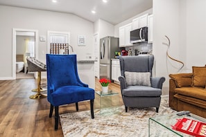 A modern living room with a blue chair, a grey armchair, and a brown sofa. There is a glass coffee table with a red tray of snacks. - Pet-Friendly & Spacious South Lubbock 3 Bed 2 Bath1 King 2 Queen Near Texas Tech (Lubbock)