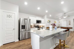 A modern kitchen with a stainless steel refrigerator, a microwave, and a built-in oven. There is a granite countertop with bar stools and a small island. - Pet-Friendly & Spacious South Lubbock 3 Bed 2 Bath1 King 2 Queen Near Texas Tech (Lubbock)
