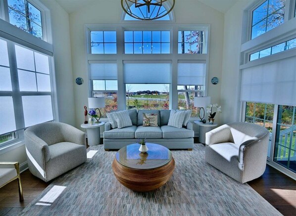 A spacious living room with a large window, a round coffee table, and a gray sofa.