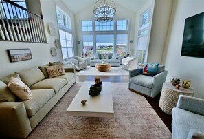 A spacious living room with a large window, a white coffee table, and a staircase.