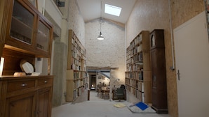 A narrow, high-ceilinged room with exposed wooden beams, large bookshelves, and a skylight. - Théveny, Le Levant (Saint-Astier)