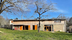 A rustic wooden house with a stone wall, a large open door, and a grassy yard. - Théveny, Le Levant (Saint-Astier)