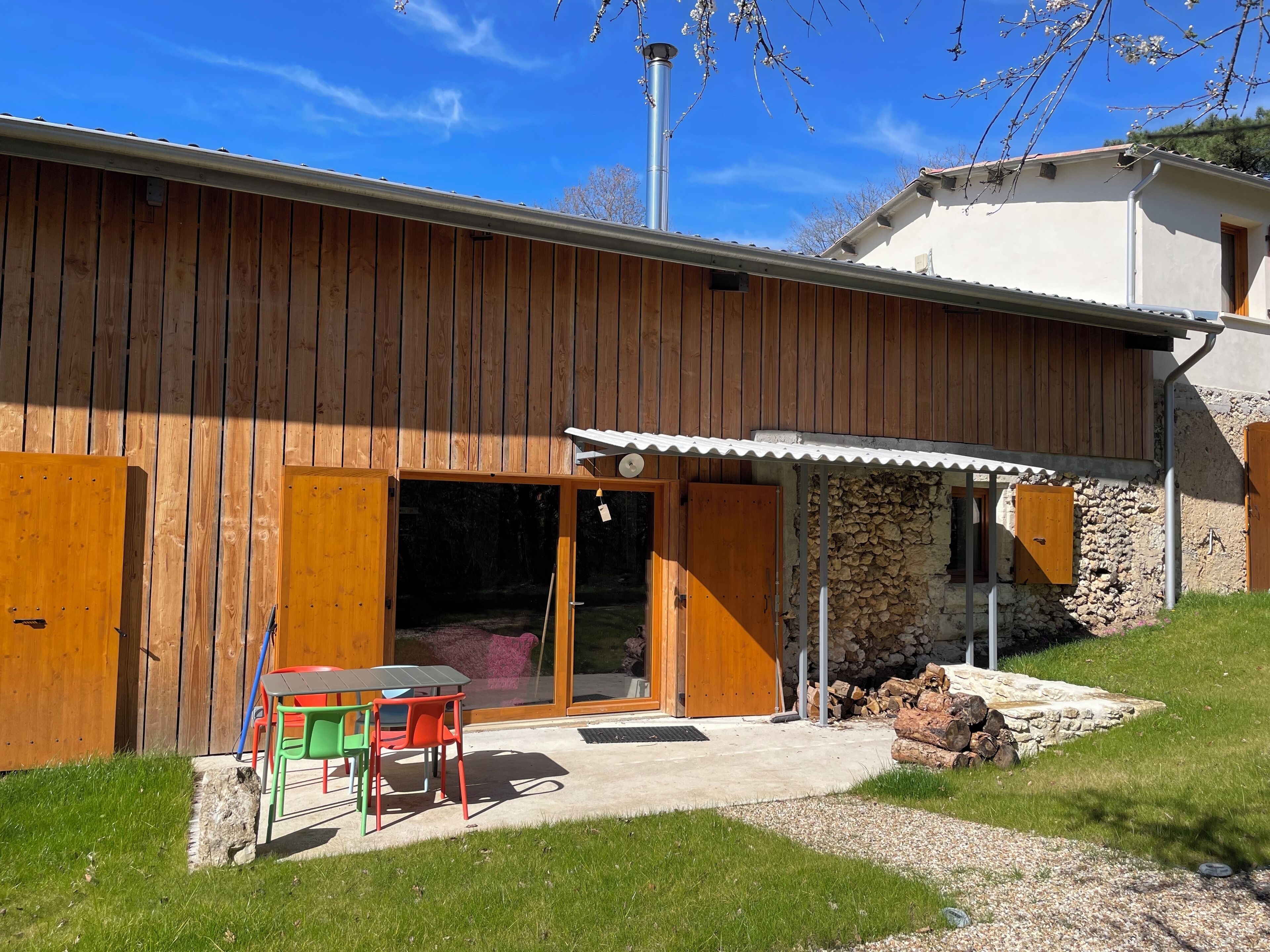 A wooden house with a stone wall, a chimney, and a patio with a table and chairs.