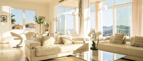 A spacious living room with a large glass coffee table, two white sofas, and a dining area with a modern chair.