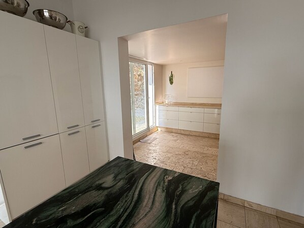 A modern kitchen with white cabinets, a marble countertop, and a view of the outdoors through a large window. - Large villa, 6 bedrooms, sea, mountain, and city views of Cannes (Le Cannet)