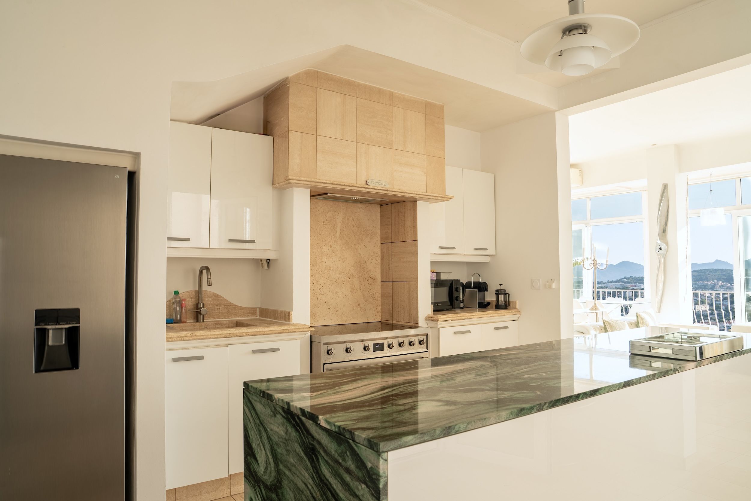 A modern kitchen with a central island, stainless steel appliances, and a view of the outdoors.