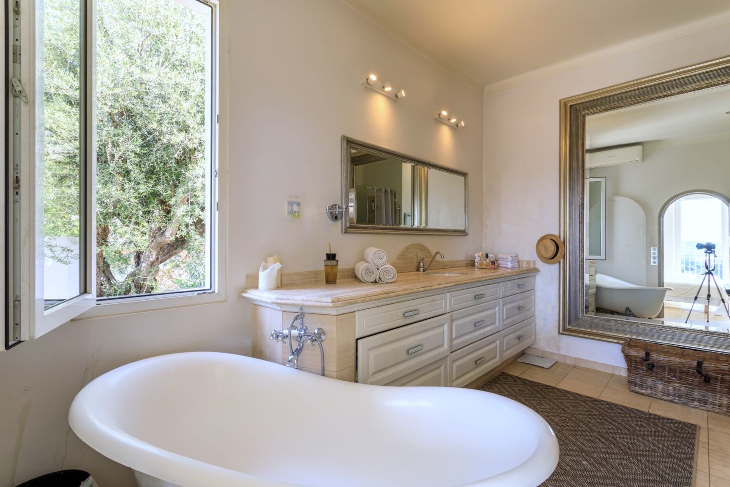 A bathroom with a freestanding bathtub, a vanity with a mirror, and a window with a view of trees.