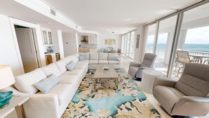 Een moderne woonkamer met een beige hoekbank, een salontafel en uitzicht op de oceaan door grote ramen.
