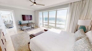 Een hotelkamer met een groot bed, een bureau met stoel, een televisie en uitzicht op de oceaan.