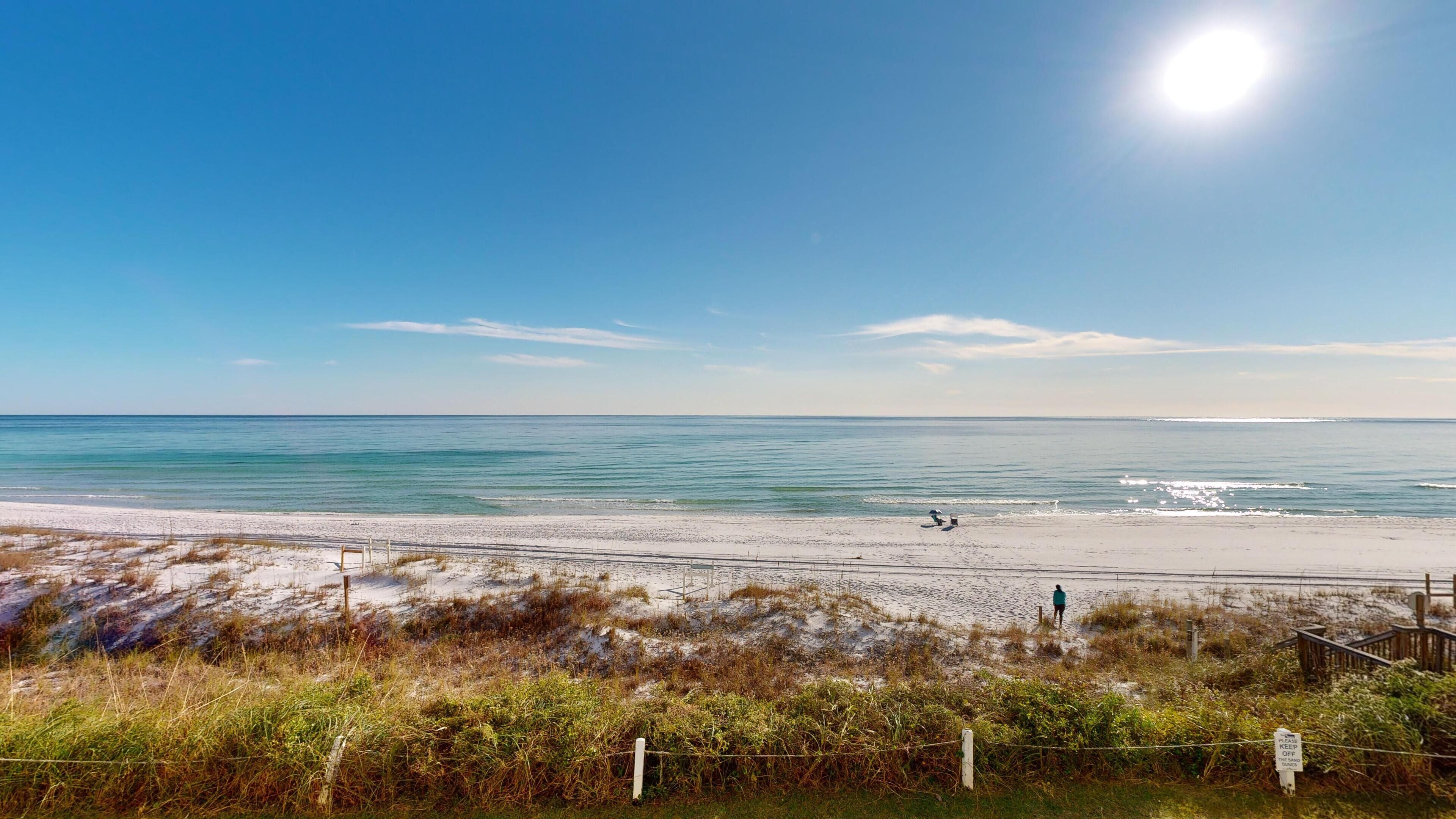 A beach with a clear sky, a sandy shore, and a person walking.