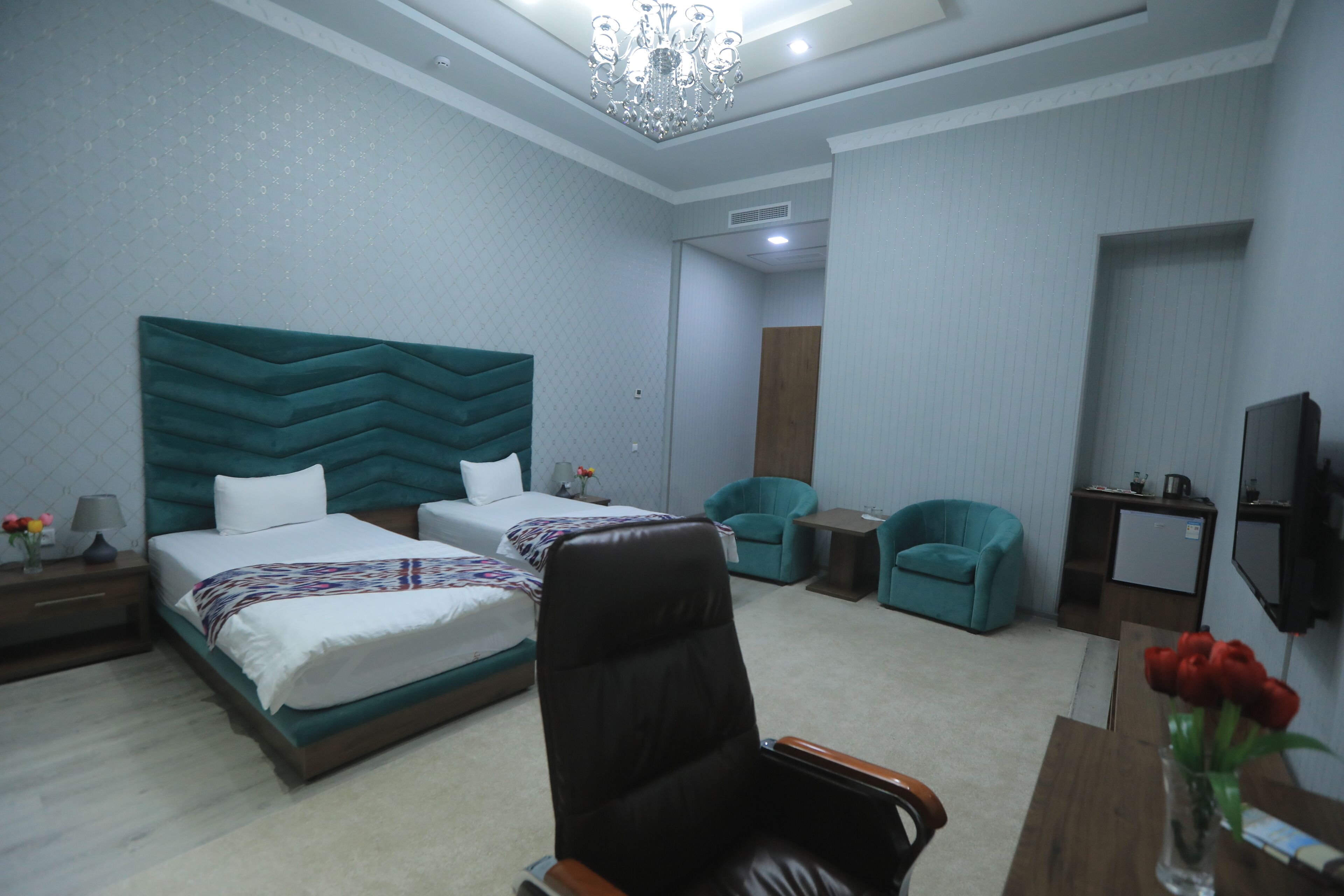 A hotel room with two beds, a desk, a chair, a TV, and a chandelier.