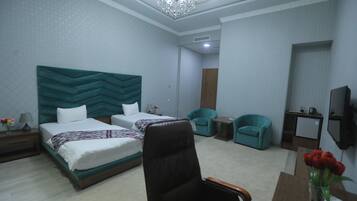 A hotel room with two beds, a desk, a chair, a TV, and a chandelier.