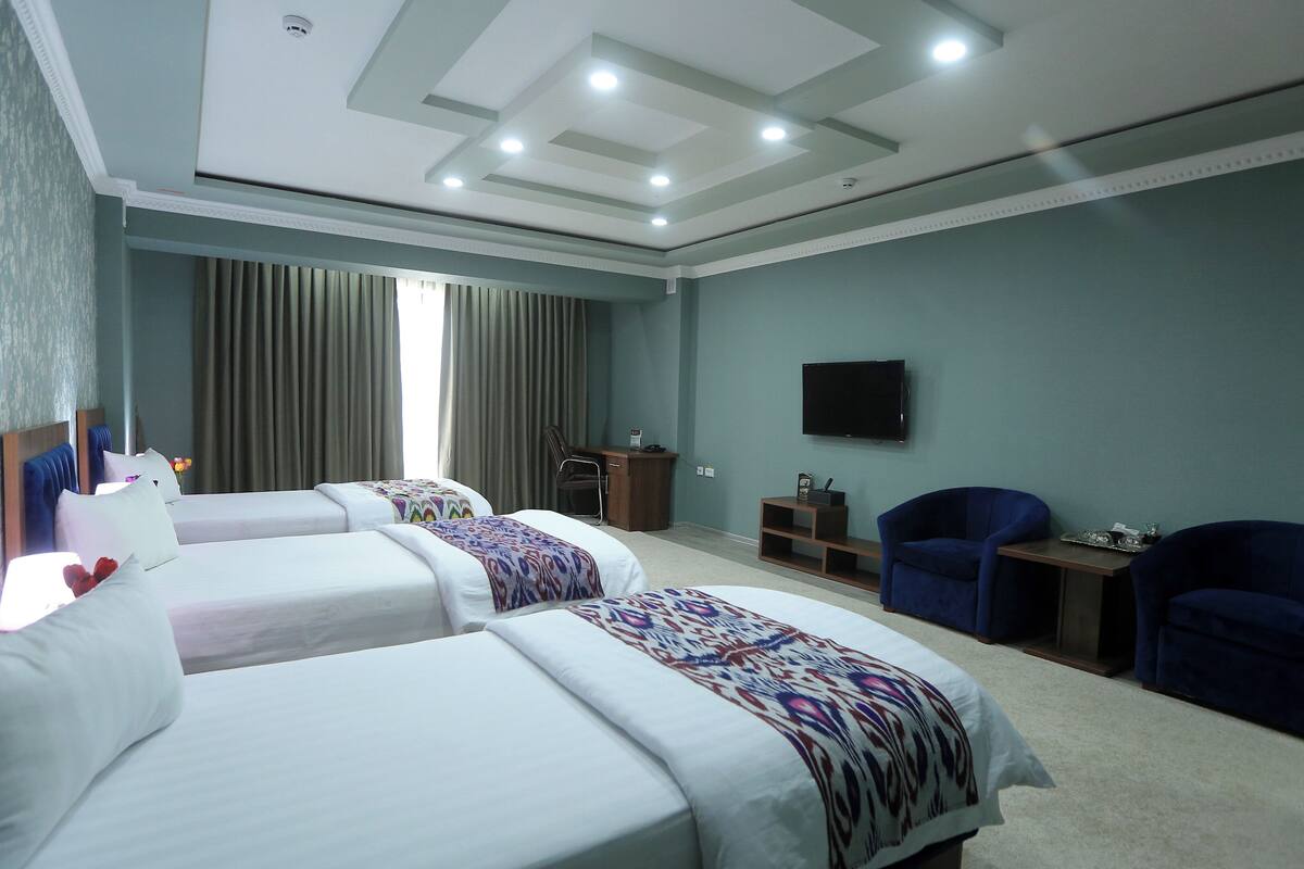 A hotel room with two beds, a desk, a chair, a TV, and a large window with curtains.
