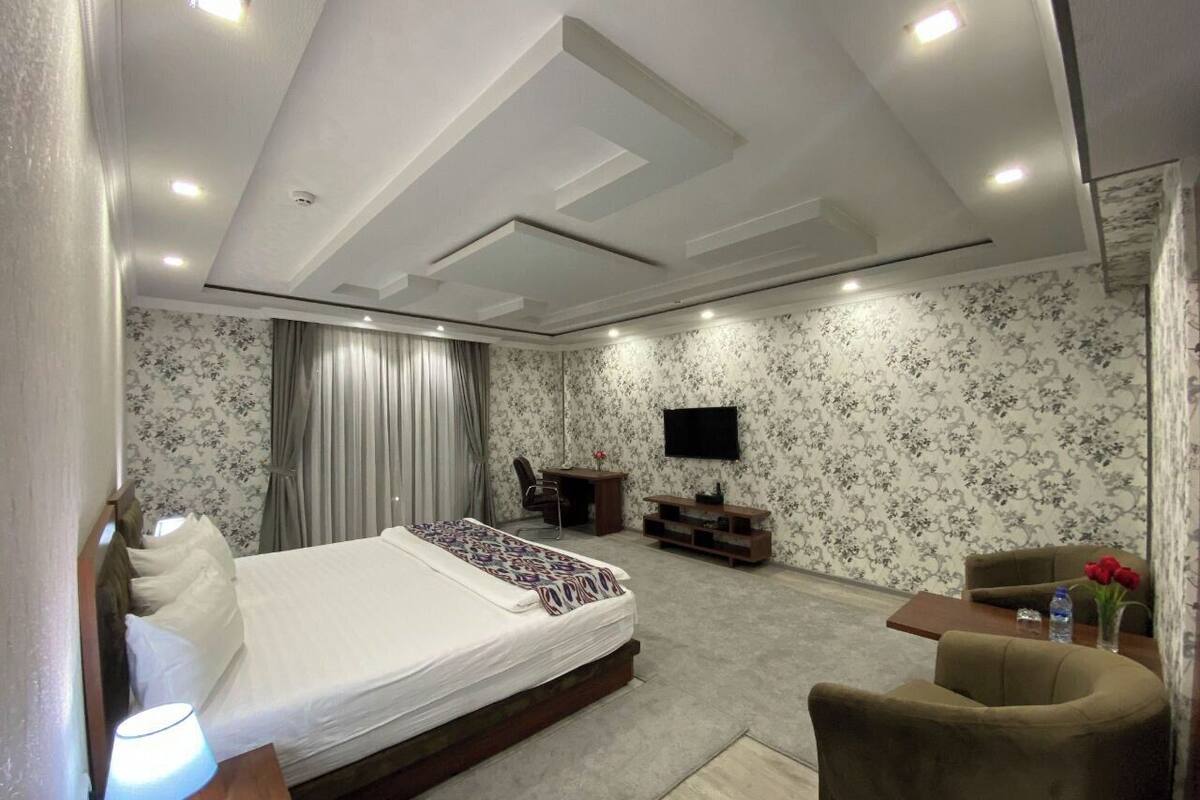 A modern hotel room with a large bed, a desk, a chair, a TV, and a small table with a vase of flowers.