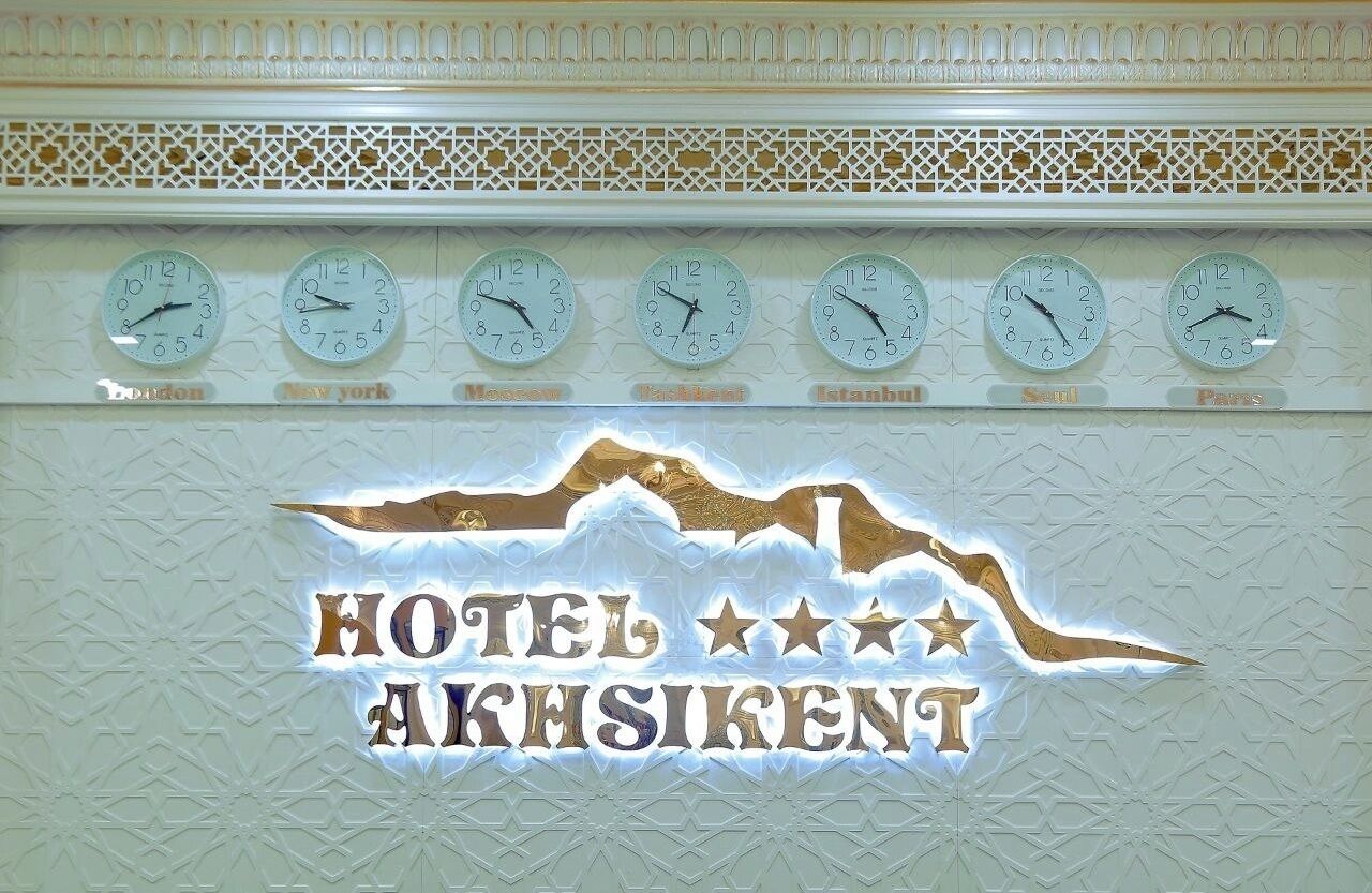 A wall with clocks set to different cities and the text "HOTEL AKHSIKENT".