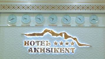 A wall with clocks set to different cities and the text "HOTEL AKHSIKENT".