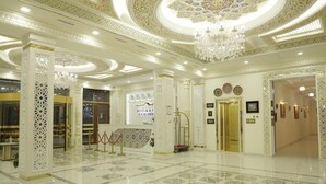 Een ruime lobby met gedetailleerde plafonddecoraties, een kroonluchter en een receptiebalie.