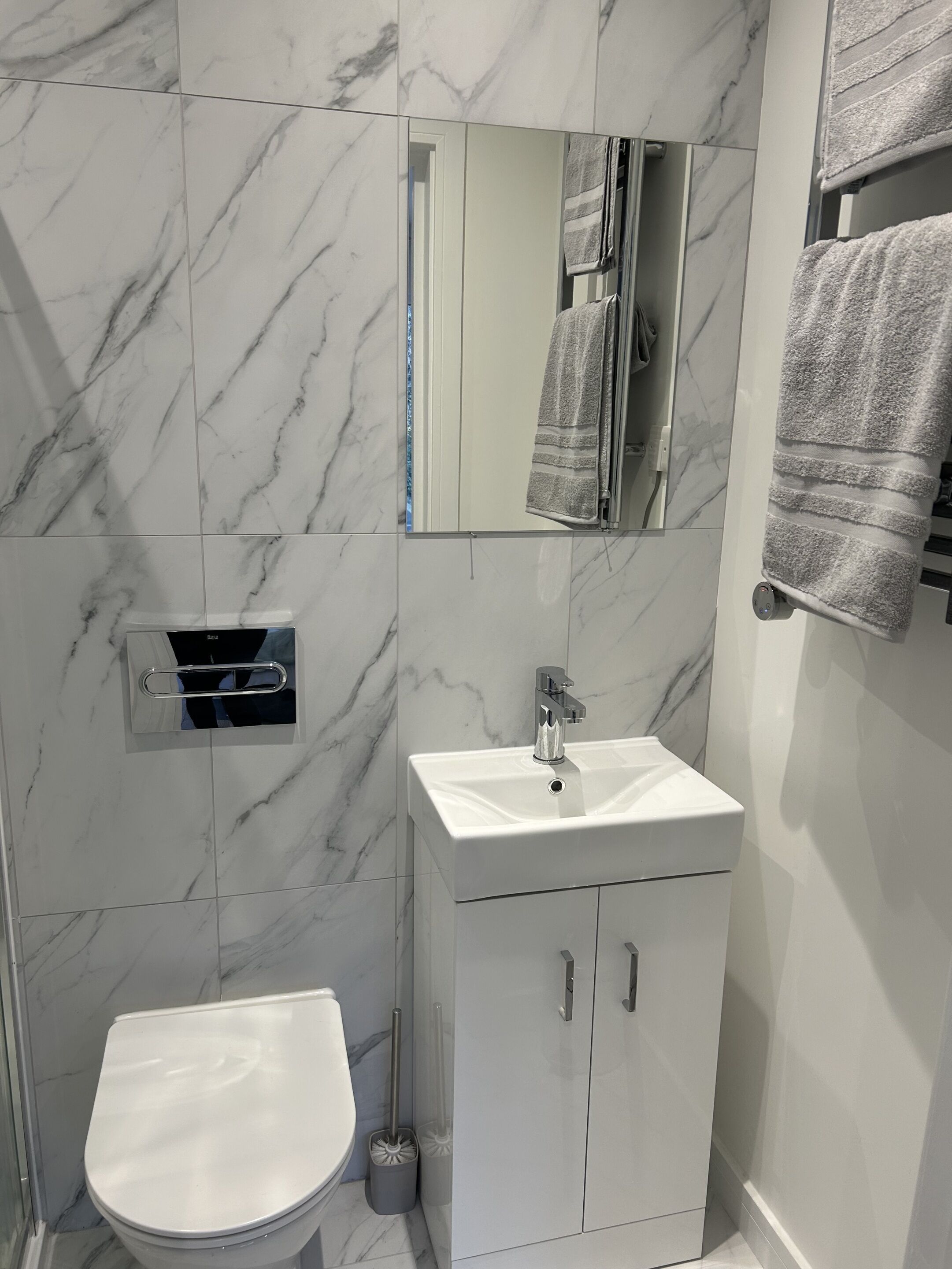 A bathroom with a white toilet, a sink with a mirror above it, and a towel rack with towels.