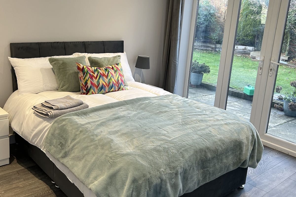 A bedroom with a large bed, a nightstand, a lamp, and a view of a garden through a sliding glass door.