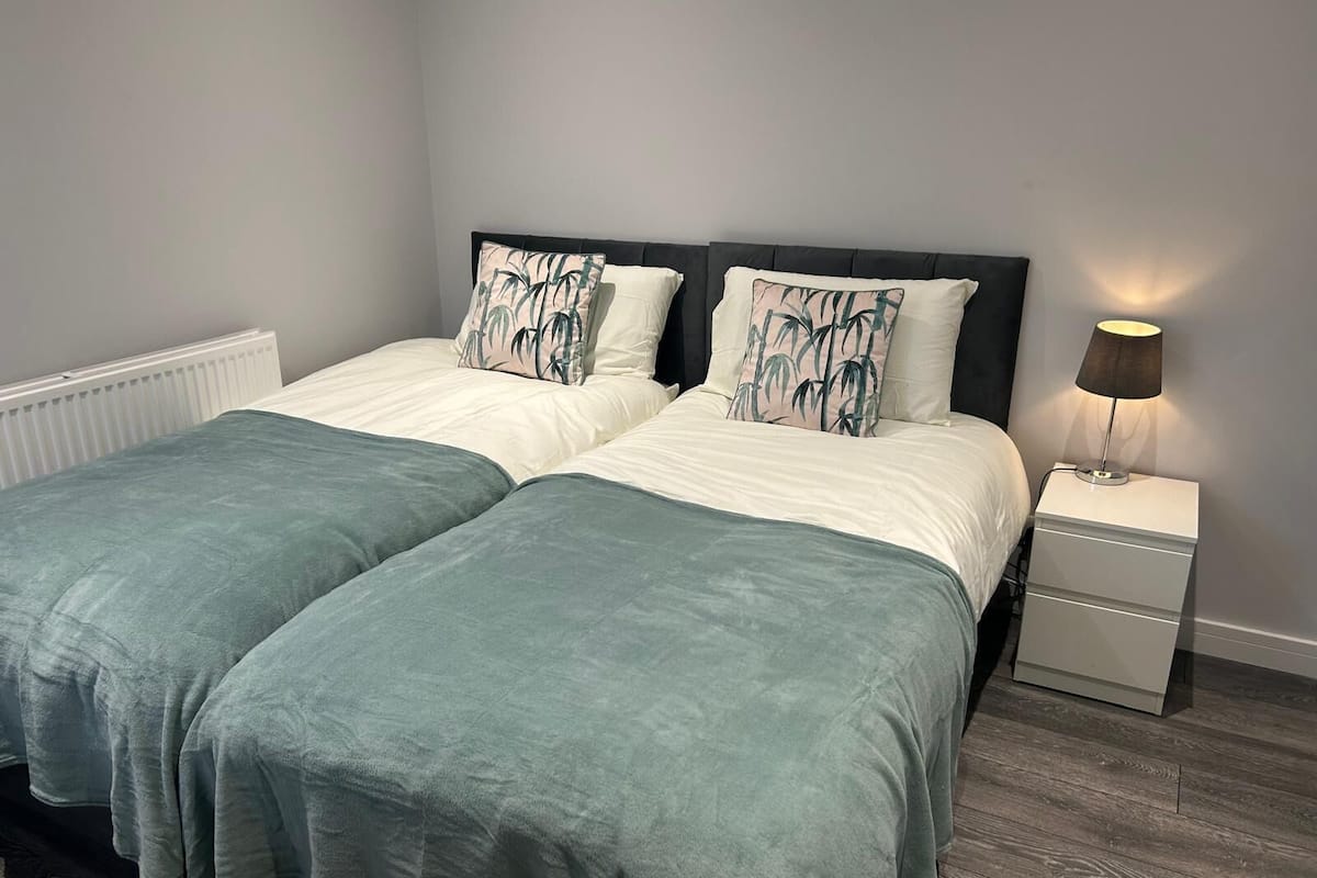 A double bed with two pillows, a bedside table with a lamp, and a radiator.