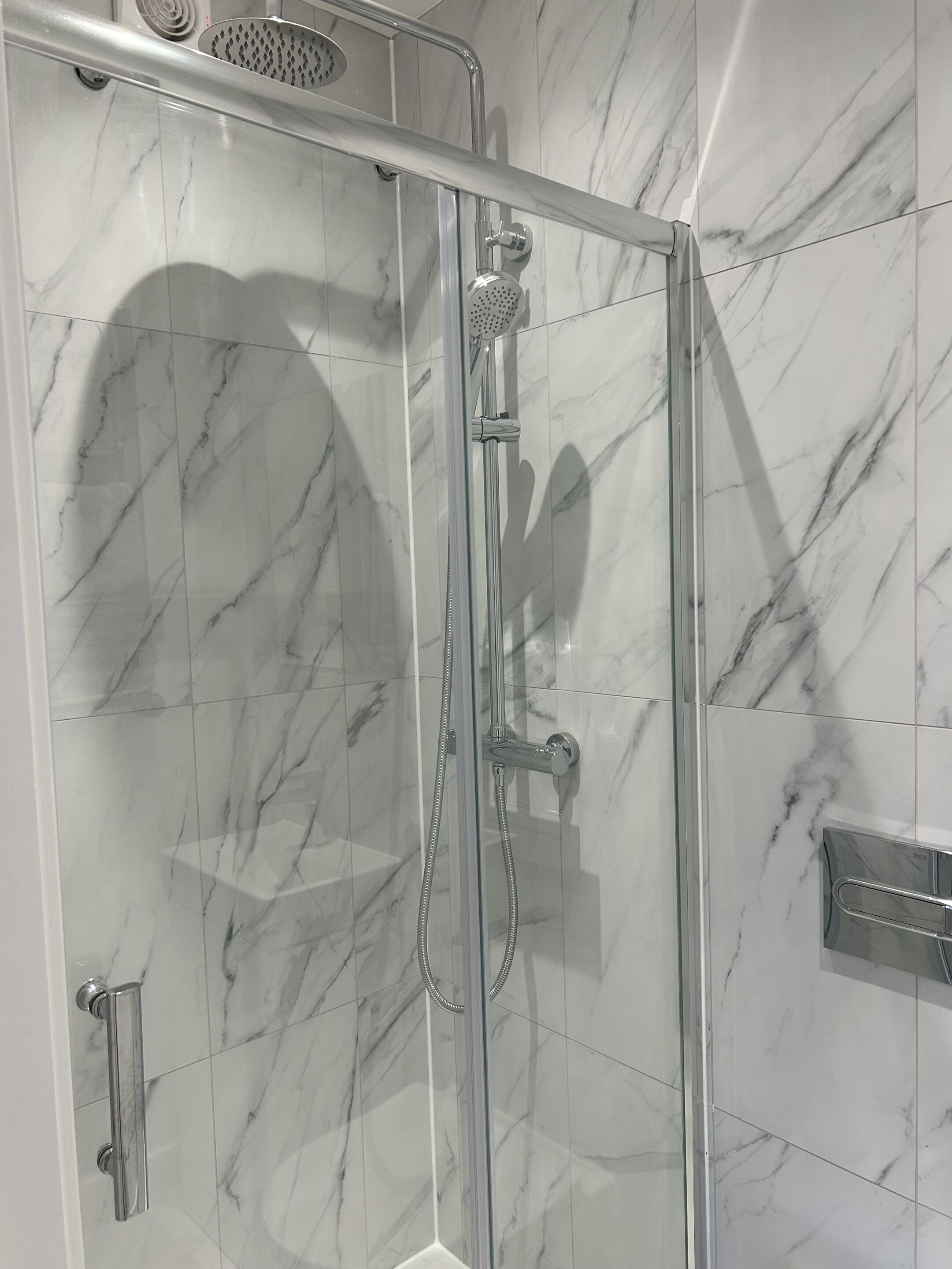 Ducha envuelta en vidrio con cabezal de ducha de mano y llave de pared.