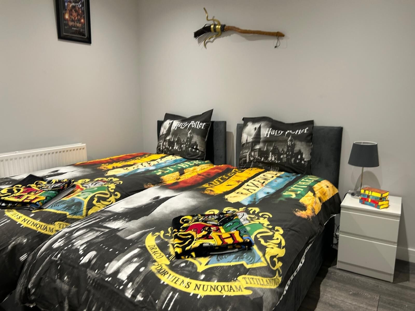 A bedroom with a bed featuring a Harry Potter-themed duvet and pillows, a bedside lamp, and a framed picture on the wall.