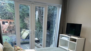 A bedroom with a large bed, a TV on a stand, and a view of the outdoors through a sliding door. - The Coniston Rooms (Kings Langley)