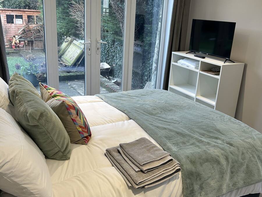 Un dormitorio con una cama grande, un televisor sobre un mueble bajo y vistas al exterior a través de una puerta corredera.