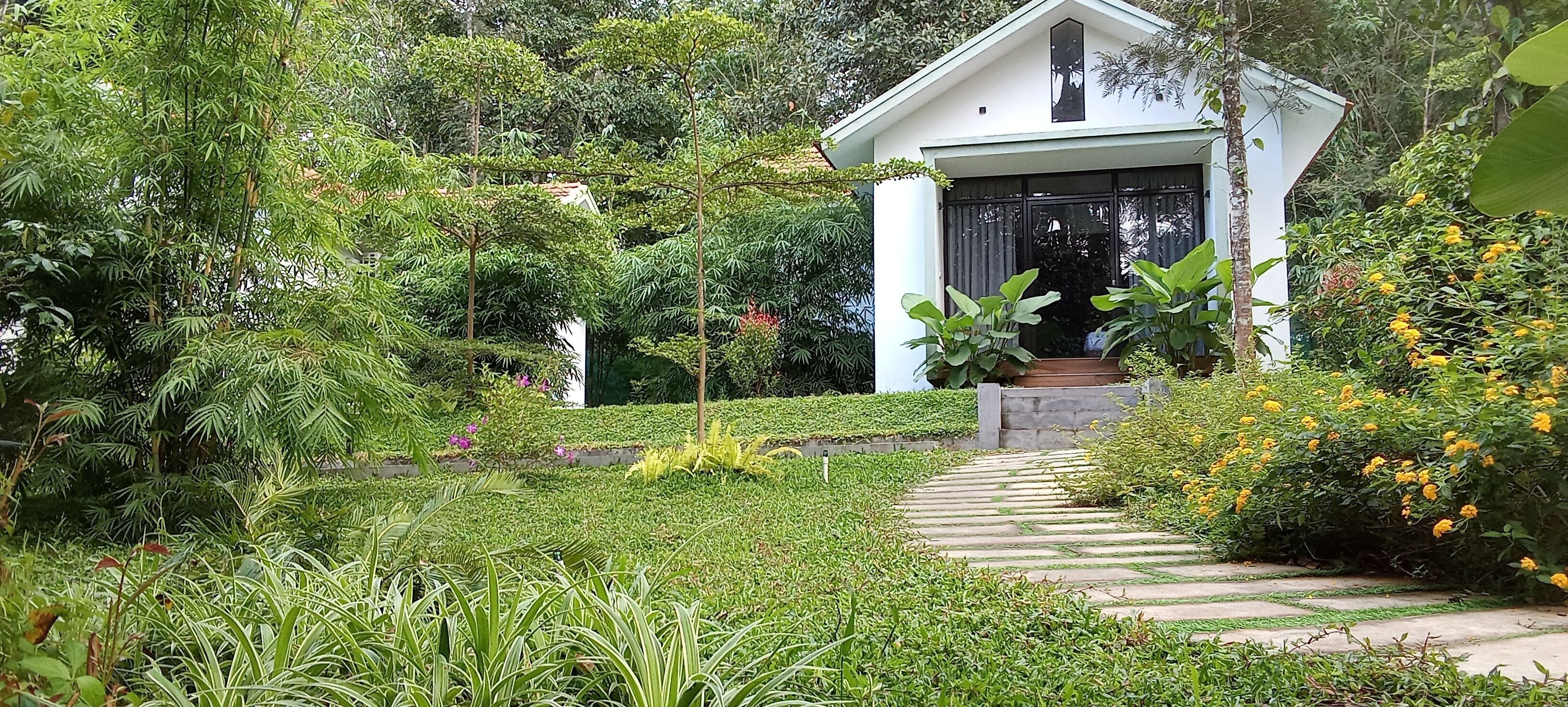 A white building with a black door, surrounded by lush greenery and a stone pathway leading to the entrance.
