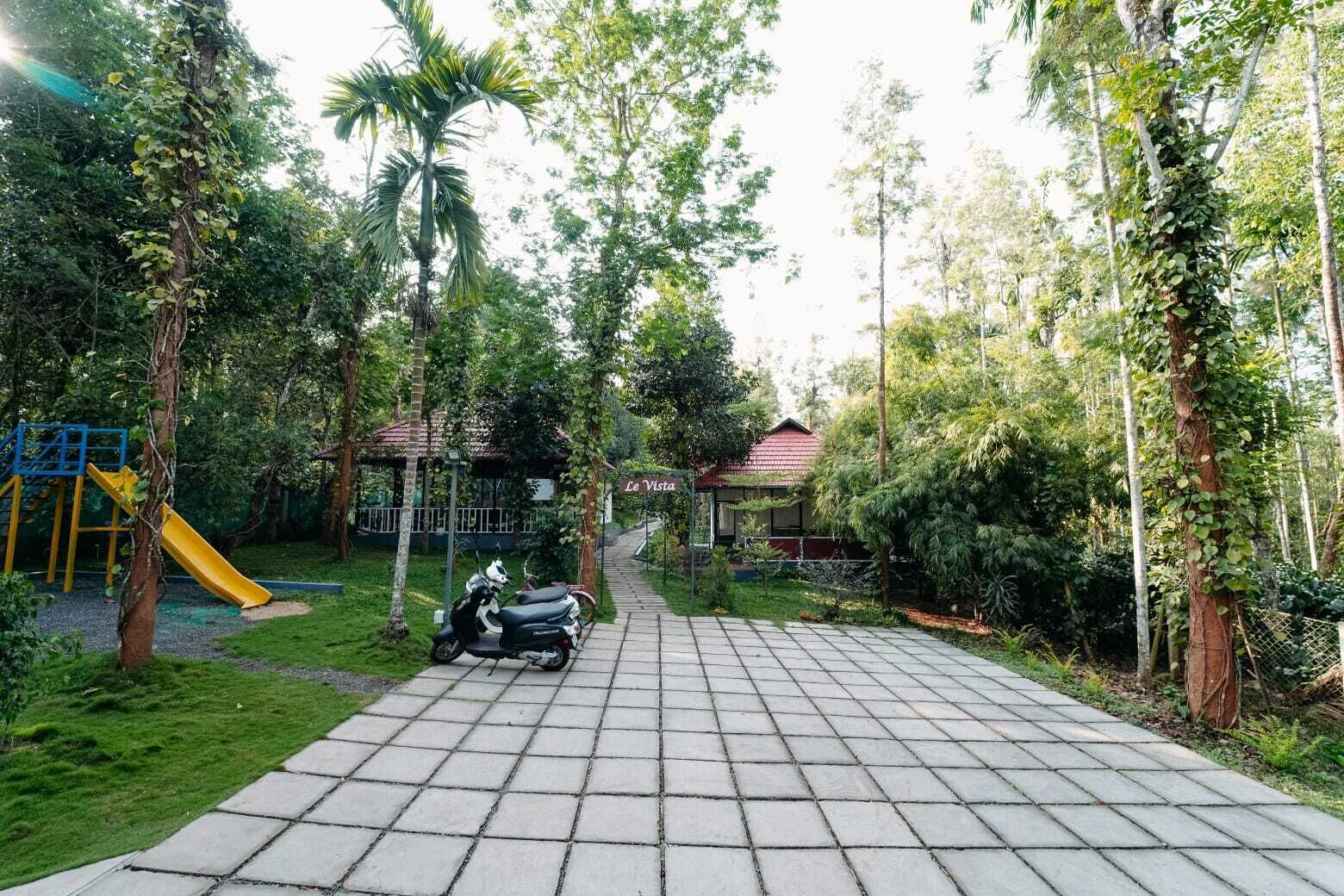 A paved pathway leading to a gazebo, surrounded by lush greenery and a playground.