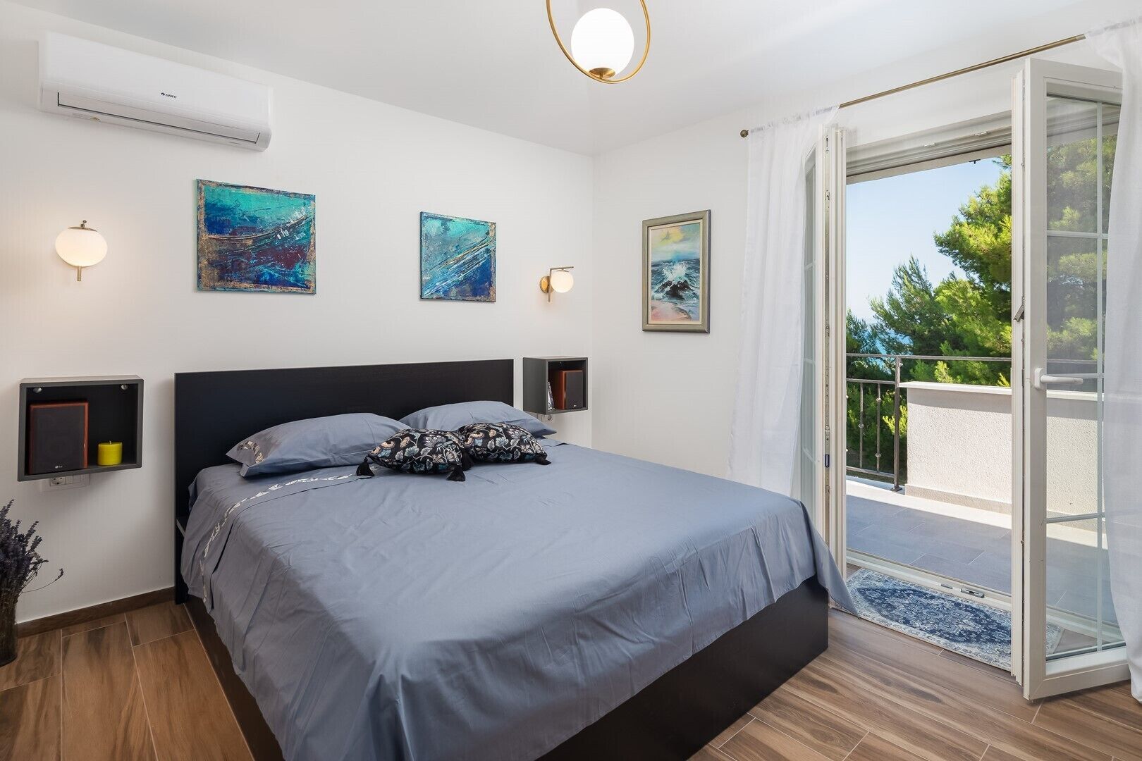 A modern bedroom with a large bed, two wall-mounted lamps, and a view of the outdoors through a sliding glass door.