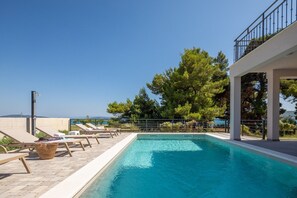Una piscina con sillas de descanso, una pérgola y vistas a árboles y montañas.