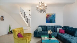 A modern living room with a staircase, a chandelier, a sectional sofa, a yellow armchair, and a colorful coffee table. - Beachfront villa Pensa with 3 en-suite bedrooms, 4th bedroom with sofa bed, private pool, playground, 6+2 people (Kastel Stafilic)