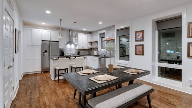 A modern kitchen with white cabinets, a central island, pendant lighting, and a dining area with a bench.