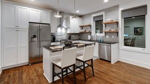 A modern kitchen with white cabinetry, stainless steel appliances, and a central island with chairs.