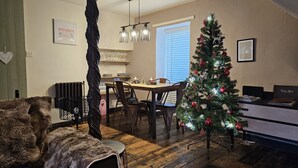 Un'accogliente zona pranzo con un albero di Natale, pavimento in legno e una cucina moderna sullo sfondo.