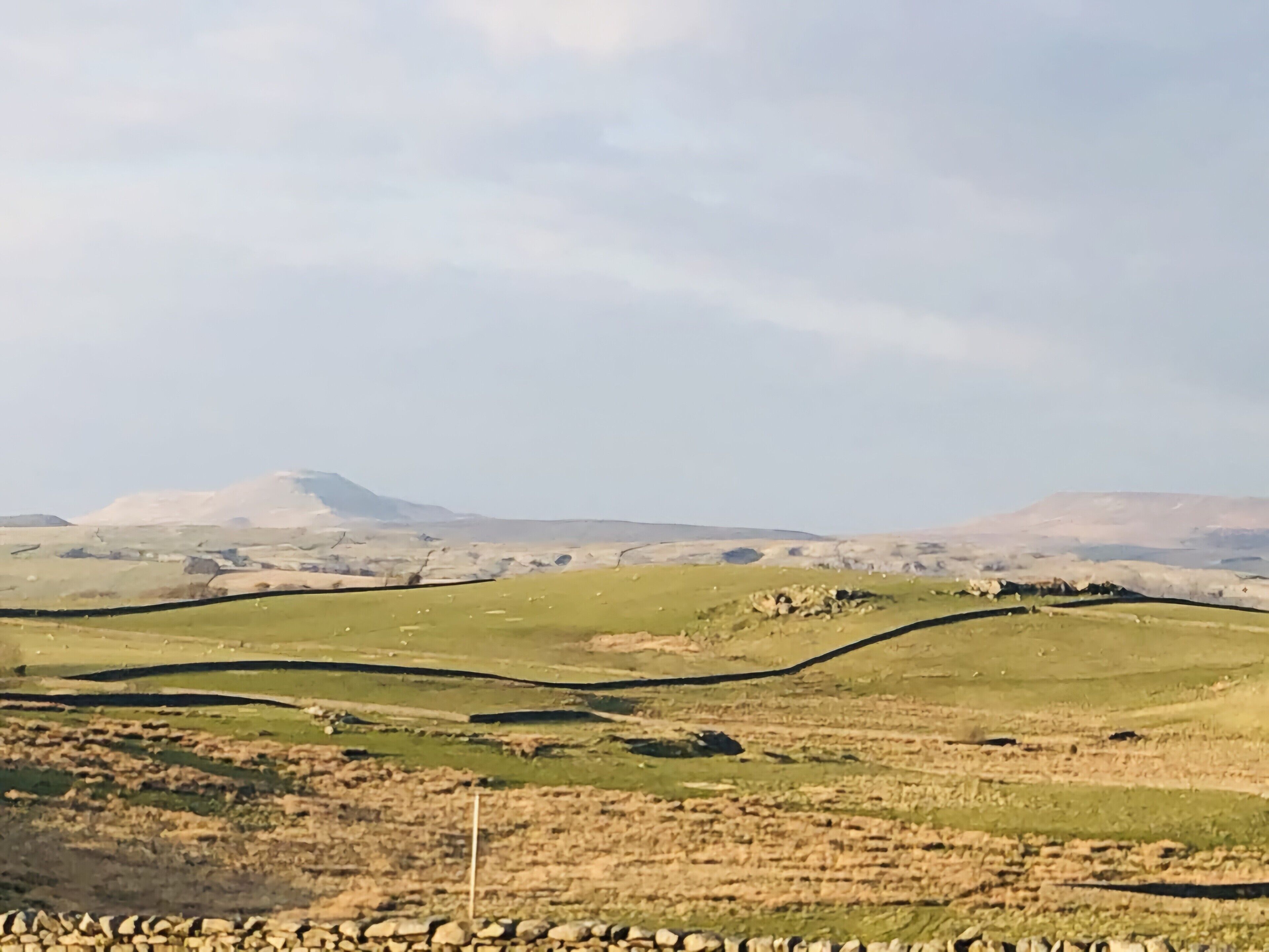 Een landelijk landschap met glooiende heuvels, stenen muren en een heldere lucht.