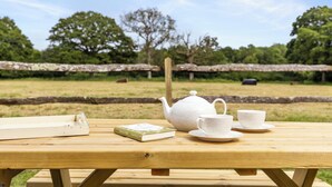 Un tavolo da picnic in legno con un bollitore, tazze, piattini e un libro.