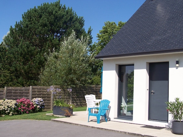 A modern house with a dark roof, a white exterior, and a grey door. There is a blue chair outside and a potted plant next to the door. - Vacation home, large garden, quiet location, near Pointe du Raz and Audierne (GOULIEN)