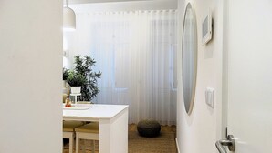 A narrow hallway with a white door, a small table with a plant, and a round mirror on the wall. - CA.Tanoeiros 1 (Funchal)